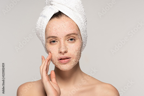 beautiful girl with towel on head applying coconut scrub on face, isolated on grey