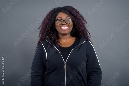 Beautiful Young African American woman with happy and funny face smiling and showing tongue. Wearing casual clothes and standing against gray studio background.