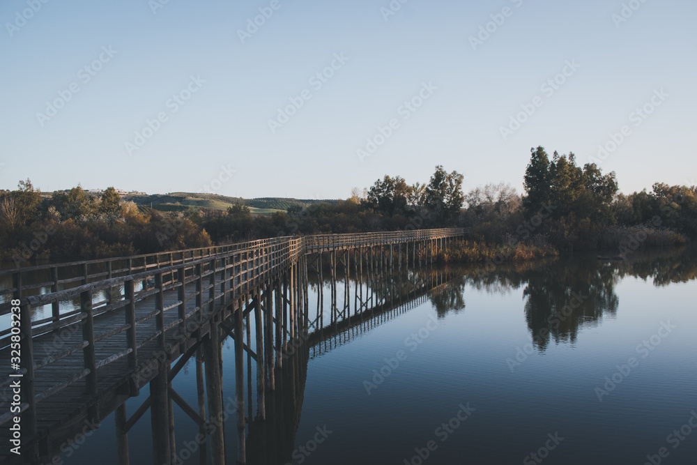 Puente de madera con su reflejo en el agua al atardecer