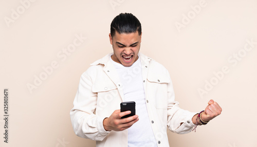 Asian handsome man over isolated background with phone in victory position © luismolinero