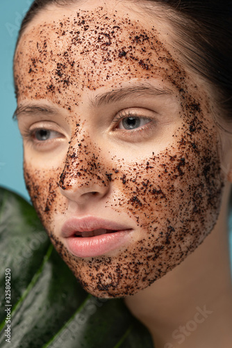 attractive girl with coffee scrub on face  isolated on blue with leaf