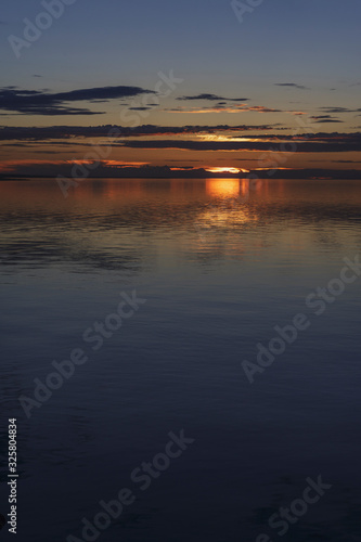 The setting sun and sky with fluffy clouds are reflected in the calm water of the lake. Traveled photo in Mongolia.