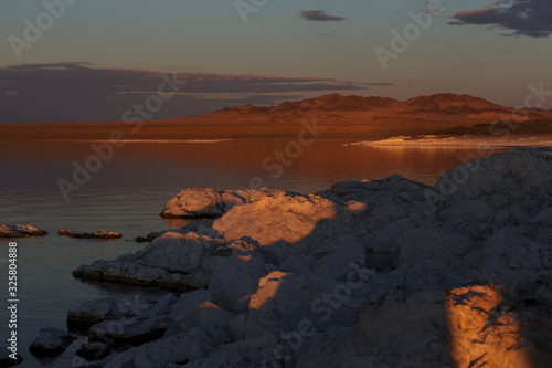 Large sharp stones lie in the lake and are illuminated by the orange light of the setting sun. Bright blue stars on a blue sky with clouds. Traveled photo in Mongolia. 