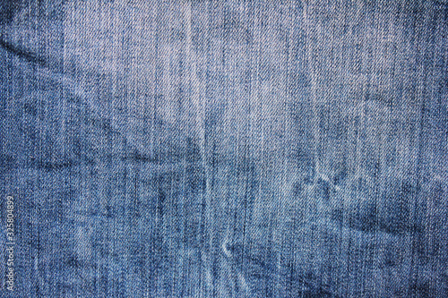 Blue jeans texture shabby worn denim trousers background. Vintage stylish light blue jean fabric surface, faded bright jeans close up top view 
