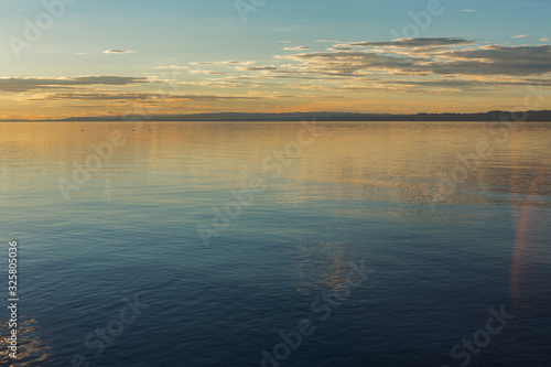 The smooth calm surface of the lake is lit by the light of the setting sun. The sky in orange tones is reflected in the water of the lake. Traveled photo in Mongolia. © rosimon