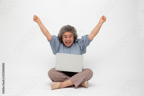 Excited senior asian woman feeling winner celebrating victory online business success and sitting on floor with laptop isolated on white background, Freelance mature concept © comzeal