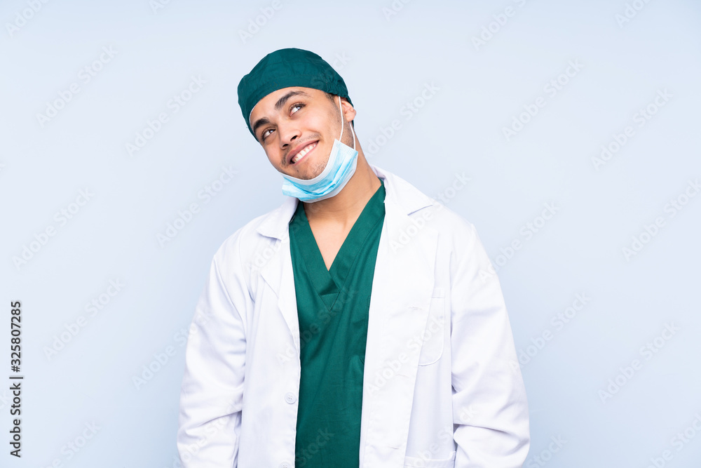 Surgeon man with uniform isolated on blue background laughing and looking up Surgeon man with uniform isolated on blue background laughing and looking up
