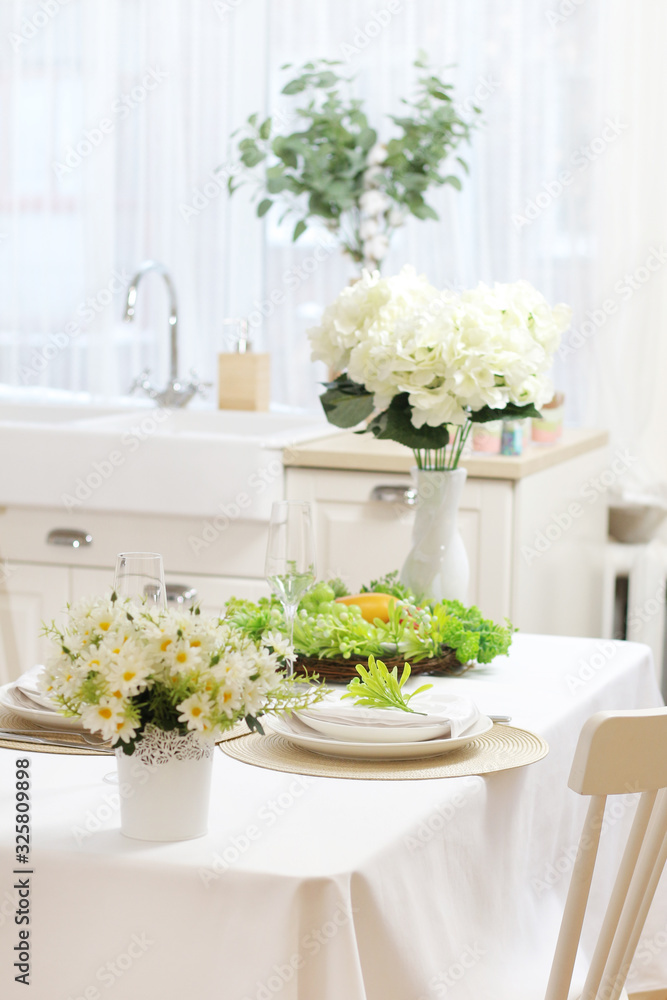 Served dining table with a white tablecloth, flowers, glasses and plates. sink by the window..