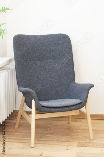 .gray armchair with wooden legs on a wooden floor near a heating battery..