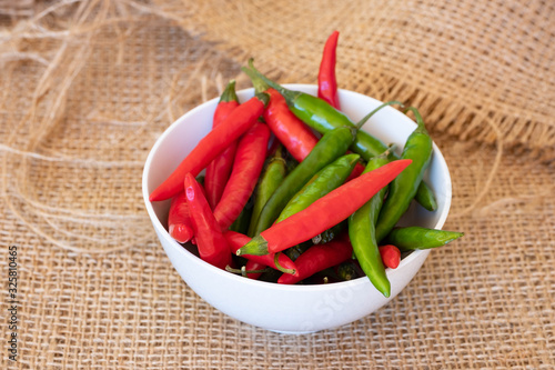 Bright red and green chillies in a white bowl on a hessian cloth.