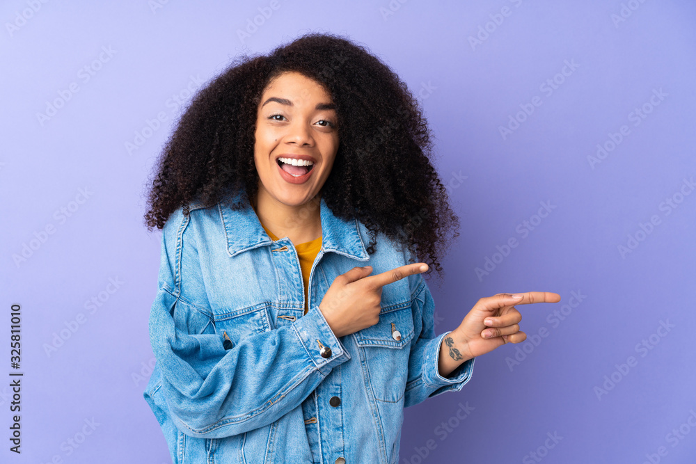 Young african american woman isolated on purple background surprised and pointing side Young african american woman isolated on purple background surprised and pointing side