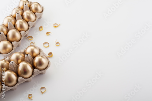 A dozen golden eggs on the edge of a white background with place for text, with copy space. Easter table concept.