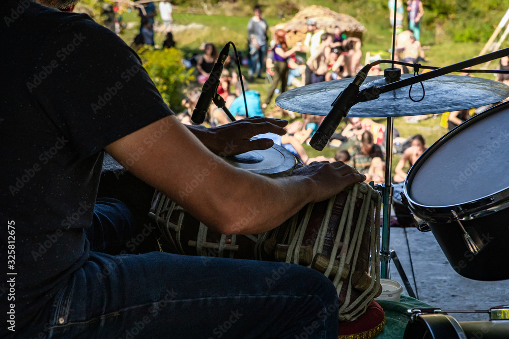 A close up selective focus shot from behind a man playing traditional drums on stage during multicultural festival, with blurry audience in background A close up selective focus shot from behind a man playing traditional drums on stage during multicultural festival, with blurry audience in background