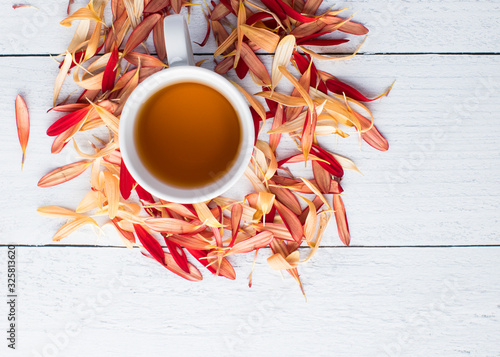 White background for text on ship lap with a pile of golden and red flower petals surrounding the tea cup photo