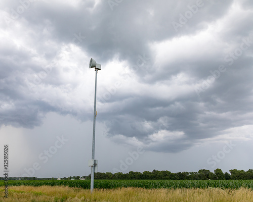 Canvas Print Severe weather alert and tornado warning siren along rural road with dark storm