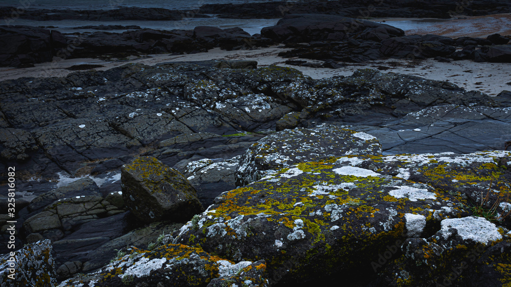 Sanna beach on west coast of Scotland on gloomy day.Black, volcanic mossy basalt rocks on diverse Scottish coastline.Dark seascape scene with atmospheric mood and blue tones.Dramatic coastal landscape