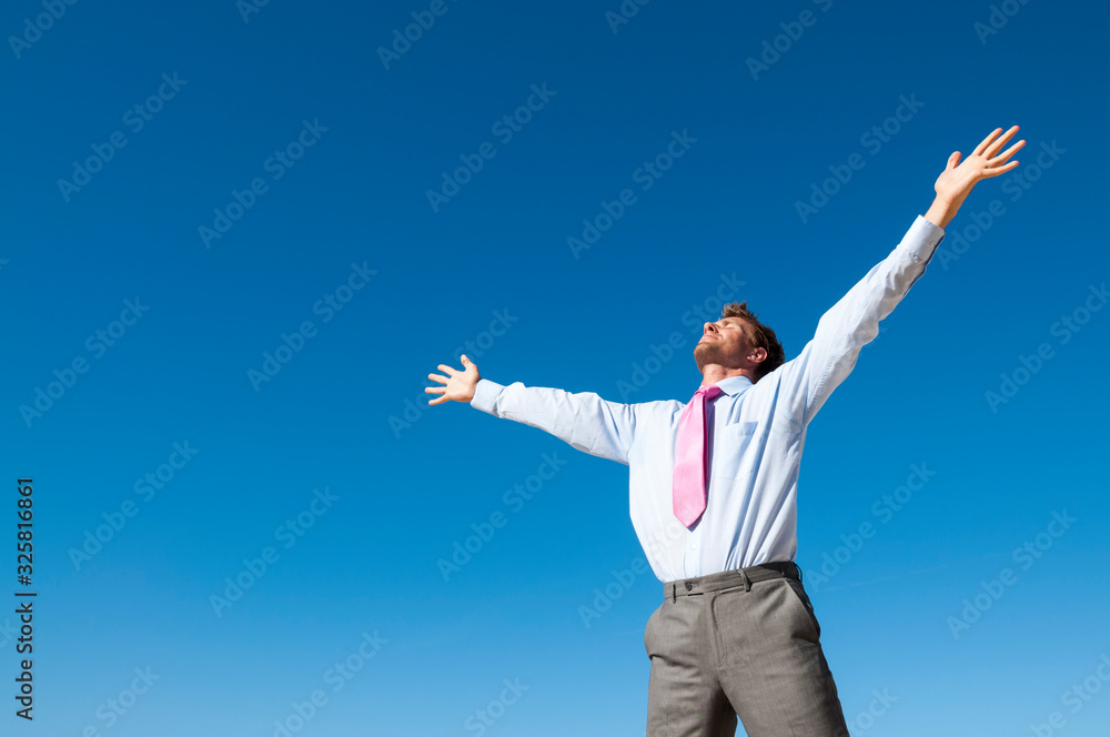 Thankful businessman standing outdoors with arms spread into the clear blue sky Thankful businessman standing outdoors with arms spread into the clear blue sky