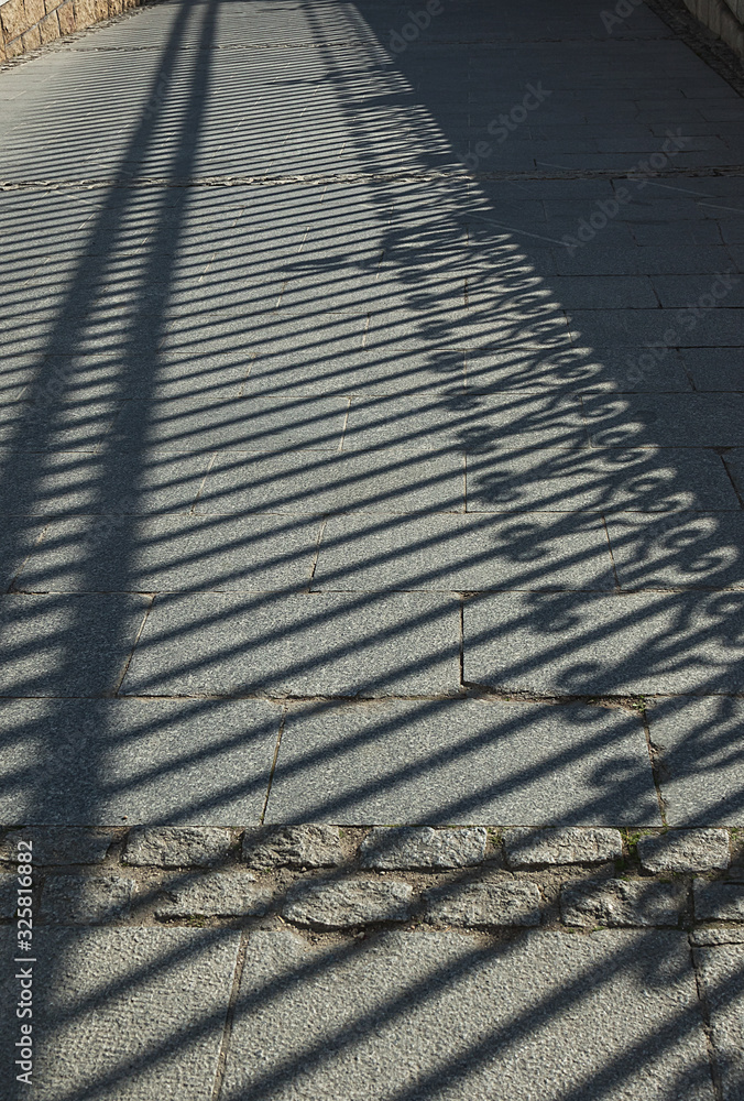 geometric diagonal shadow from an old fence on a path from paving slabs. Background from light and shadow.