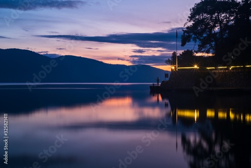 Mountains, rays and fishing man reflected in the sea at sunset. Tulle appeara...