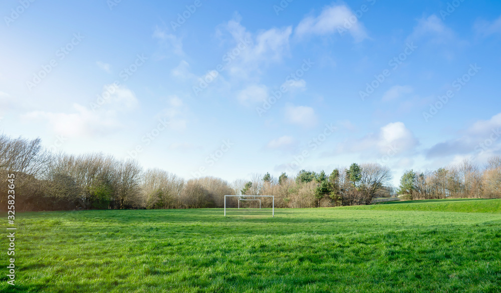 Panoramic view of football pitch in sunny day early spring, Landscape of football field at the end of winter. Goal posts on green grass with cloudy and blue sky.