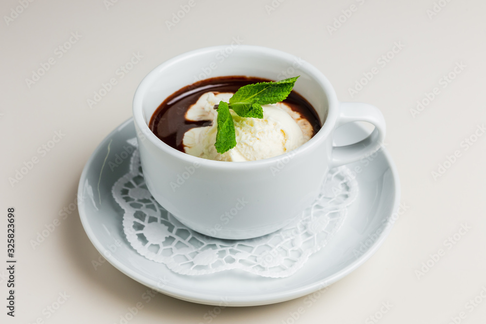 A small white cup of dark hot chocolate with vanilla ice-cream and mint on a white saucer and a napkin A small white cup of dark hot chocolate with vanilla ice-cream and mint on a white saucer and a napkin