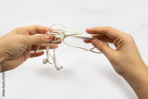 male hands are holding white headphones with tangled wires