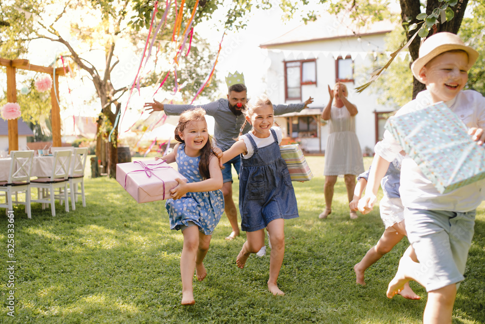 Obraz premium Small children ruunning with present outdoors in garden on birthday party.