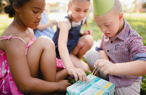 Down syndrome child with friends on birthday party outdoors, opening presents.