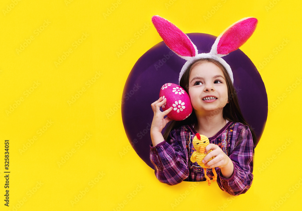 Funny happy child girl with Easter eggs and bunny ears on yellow