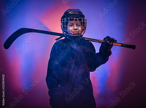 Canvas Print Young blonde sporty boy, ice hockey player, posing in a bright neon studio for a