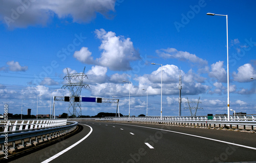 Image of Empty Freeway  under a bright blue sky. Long asphalt road with white lines down the centre . Travel and transportation concept. Travel .