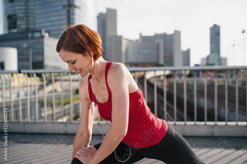 Young woman runner with earphones in city, stretching. © Halfpoint