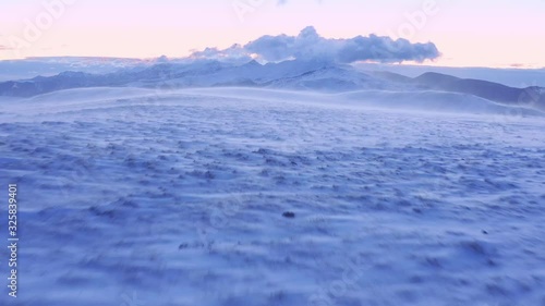 Aerial Flight Over Snow Blowing In Mountain Winter Hills Golden Hour Colors Colorful Purple Orange Sky Cold Weather Cinematic Flight 4k photo