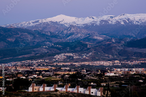 landscape with snowy mountains and valley with houses at sunset