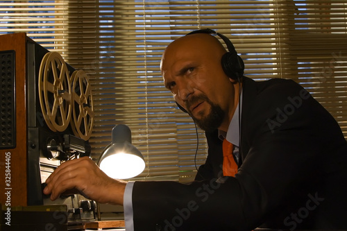 Obraz na plátně A male spy listens and records conversations on a reel-to-reel tape recorder, intelligence and spying on citizens, and a super-agent with headphones