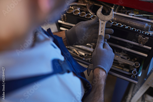 High angle close up of car mechanic holding wrench while choosing tools in garage shop, copy space