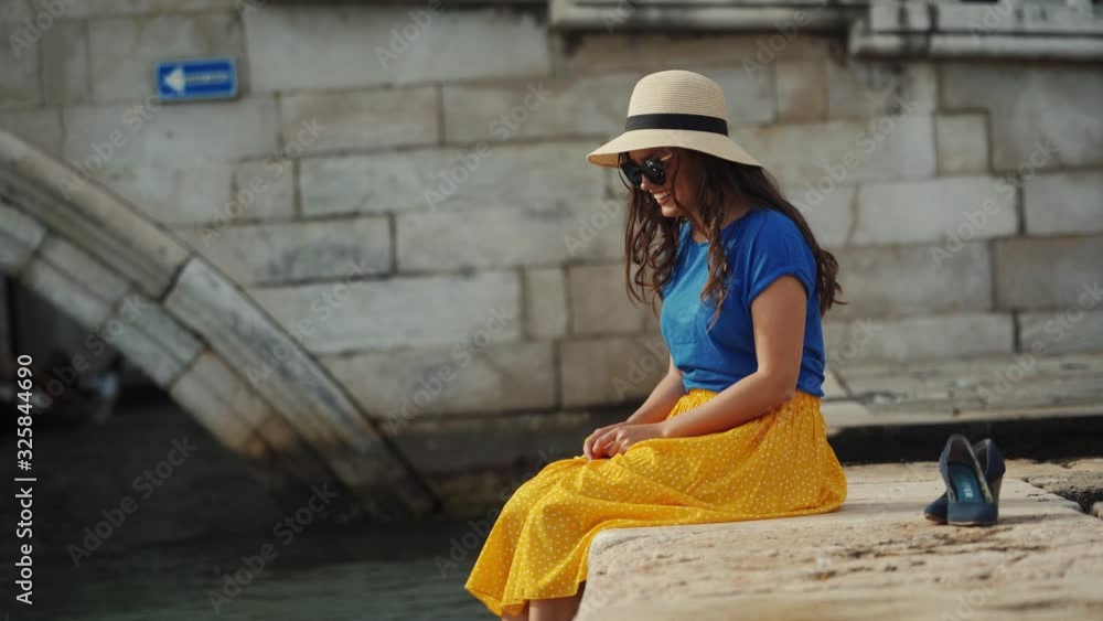 Close-up of barefoot female legs on canal. Girl in yellow skirt splashes water Close-up of barefoot female legs on canal. Girl in yellow skirt splashes water