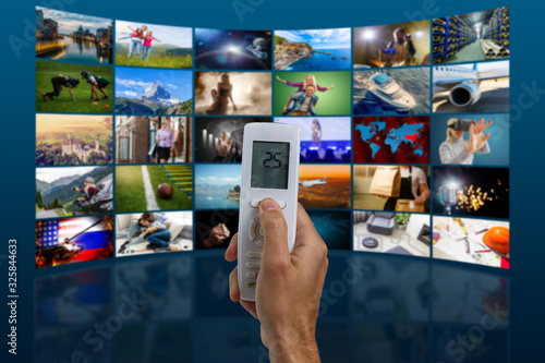 Hands holding remote control with different online subscription apps on TV screen in out of focus © Angelov