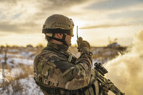 Ukraine war soldier army Man in multicam camouflage speaks on the walkie-talkie radio. equipment commandos with helmet and gun. soldier, sun backlight and smoke. modern warfare. atmosphere of battle