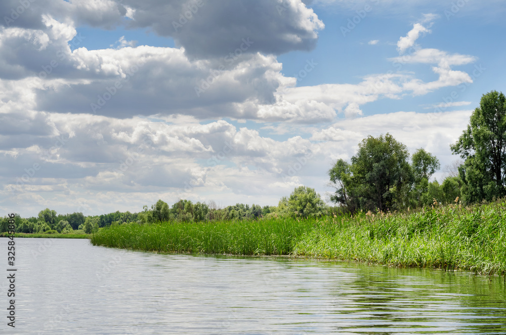 Summer river landscape with uninhabited coast and blue sky with clouds