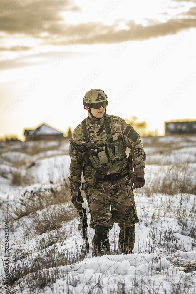 Fototapeta premium equipped army soldier Man in the winter multicam camouflage is patrolling or patrol field territory. commandos with full equipment helmet and gun watch battlefield. Modern army soldier