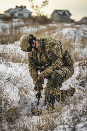 soldier man in the winter multicam camouflage opens up or drills and prepares a smoke bomb