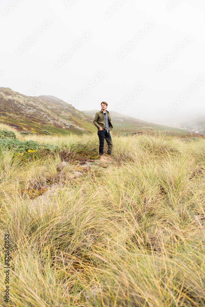 Young man standing in field of sea grass on the coast Young man standing in field of sea grass on the coast