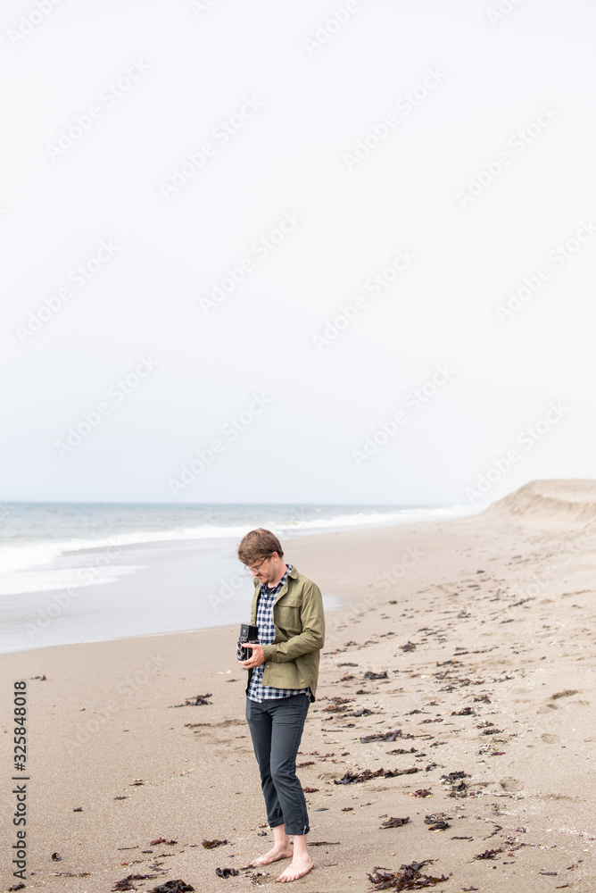 Young man standing on beach taking photograph with film camera Young man standing on beach taking photograph with film camera