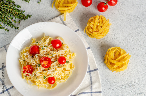 Homemade tagliatelle pasta with tomatoes, thyme, parmesan cheese in a white plate on a light background