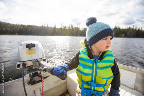 Young boy driving motor boat on calm lake on sunny day.