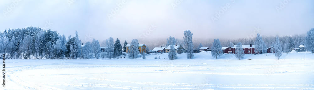 Very wide panorama view on Swedish village with red and yellow wooden houses in winter overcast on frozen river coast at spruce forest edge, Lappland, Scandinavia. Very wide panorama view on Swedish village with red and yellow wooden houses in winter overcast on frozen river coast at spruce forest edge, Lappland, Scandinavia.
