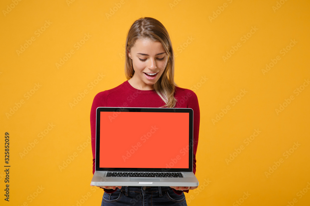 Pretty young blonde woman girl in casual clothes posing isolated on yellow orange background in studio. People lifestyle concept. Mock up copy space. Hold laptop pc computer with blank empty screen. Pretty young blonde woman girl in casual clothes posing isolated on yellow orange background in studio. People lifestyle concept. Mock up copy space. Hold laptop pc computer with blank empty screen.