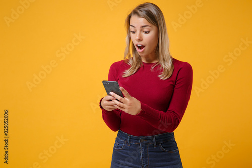 Excited young blonde woman girl in casual clothes posing isolated on yellow orange wall background studio portrait. People lifestyle concept. Mock up copy space. Using mobile phone typing sms message.