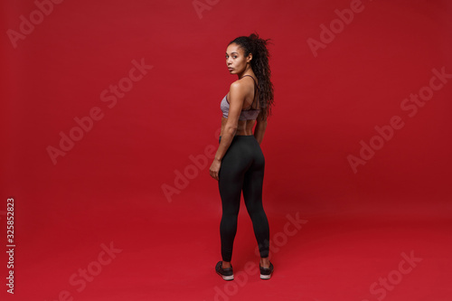 Fotografia Back rear view of young african american sports fitness woman in sportswear posing working out isolated on red background studio portrait